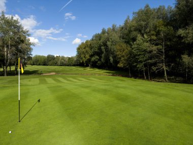 Bayrak ve golf kulübündeki delik. Mavi gökyüzü. Yaz günü bulutlu.