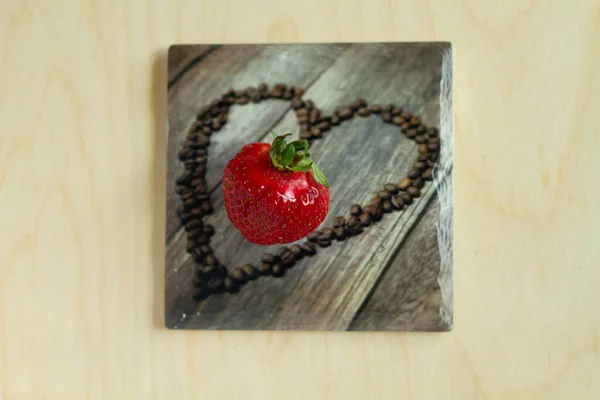 single fresh strawberry fruit on a cup pad with a heart shaped coffe grains as a picture