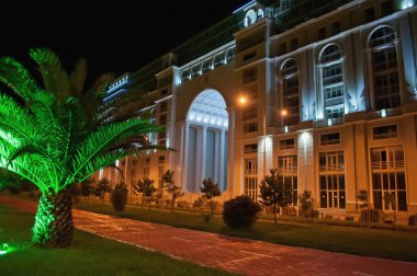 Otelin ön cephesi aydınlandı. Batumi şehrinde bisiklet yolu olan bir set. Georgia 'da gece hayatı. Akşam mimari çekimi.