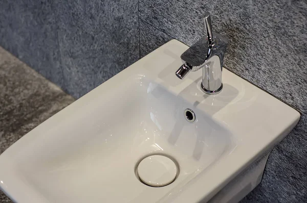 Bidet sospeso con miscelatore cromato su sfondo di piastrelle grigie. Impianti idraulici per il bagno moderno — Foto Stock