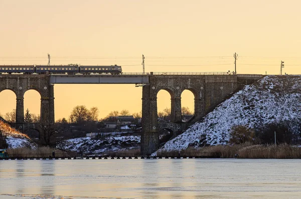 Train passant sur un vieux pont surplombant la rivière, rivière d'hiver dans la glace et la neige. Pont ferroviaire en pierre avec arches, viaduc à Kropyvnytskyi — Photo