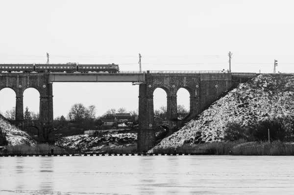 Pociąg przejeżdżający przez stary most nad rzeką, zimowa rzeka w lodzie i śniegu. Kamienny most kolejowy z łukami, wiadukt w Kropiwnickim — Zdjęcie stockowe