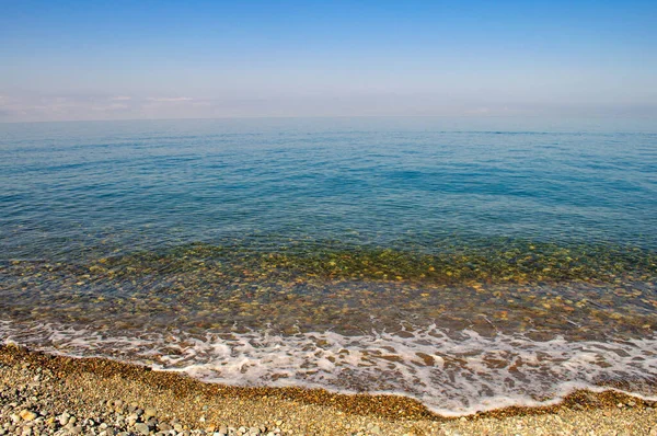 Καλοκαίρι θαλασσογραφία με λείο νερό και γραμμή ορίζοντα, καθαρό γαλάζιο νερό. Παραλία με βότσαλα σε μια ηλιόλουστη μέρα, μικρά κύματα — Φωτογραφία Αρχείου