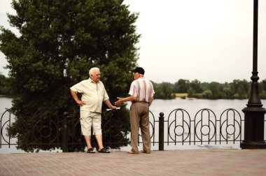 Kyiv, Ukraine. June 27. 2013. Emotional conversation of two elderly men near the fence on the waterfront. clipart