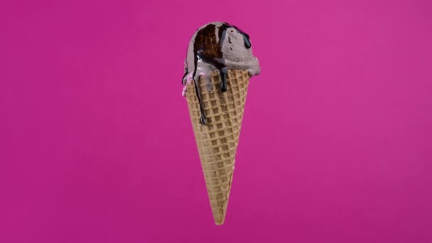 Deliciosa bola de helado de chocolate con cobertura de almíbar en cono de gofre sobre fondo rosa. Crema suave giratoria, helado helado cucharada en cono de gofre sobre fondo colorido — Vídeos de Stock