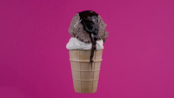 Tasty chocolate and vanilla ice cream balls with syrup topping in waffle cone on pink background. Rotating soft cream, gelato icecream scoop in waffle cone over colorful background — Video Stock