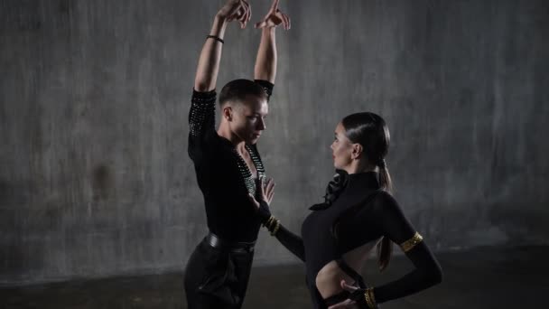 Joven y elegante pareja de baile de salón con vestido negro bailando tango en pose sensual sobre fondo grunge. Bailarinas profesionales perfumes latino. Emociones humanas, amor y pasión — Vídeos de Stock