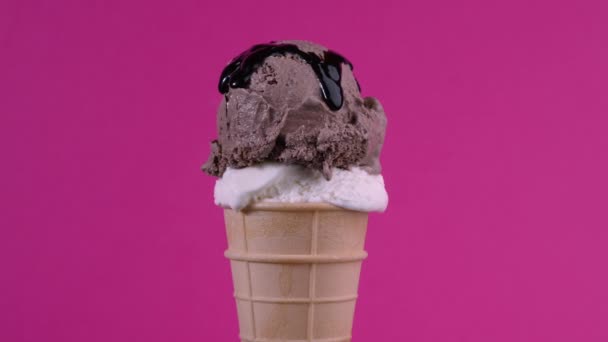 Deliciosas bolas de helado de chocolate y vainilla con cobertura de almíbar en cono de gofre sobre fondo rosa. Crema suave giratoria, helado helado cucharada en cono de gofre sobre fondo colorido — Vídeos de Stock