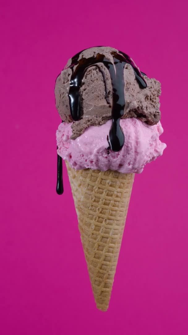Tasty chocolate and strawberry ice cream balls with syrup topping in waffle cone on pink background. Rotating soft cream, gelato icecream scoop in waffle cone over colorful background — 图库视频影像