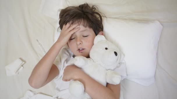 Sick child boy with fever lying on pillow in bed with teddy bear. Tired lack of energy preschool kid, temperature, fever flu symptoms and treatment, children medical healthcare, corona virus symptoms — Vídeo de stock