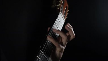 Erkek eller klasik akustik gitar çalar, akorları öğrenir, kendi kendini eğiten telli çalgılar çalar. Profesyonel müzisyen siyah arkaplan üzerinde mükemmel bir teknik sergiliyor.
