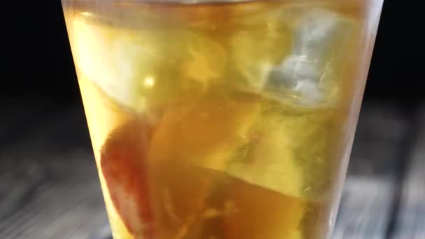 Rotating peach iced tea in the glass with fruit slices and ice cubes. Healthy refreshing lemonade for detoxification, sweet tasty soft drink or cold aromatic beverage for summer time in slow motion — Vídeo de Stock