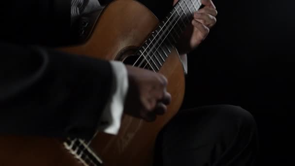 Male hands plays the classical acoustic guitar, learning chords, self-educating playing string instrument. Professional musician performing melody showing excellent technique over black background — 비디오