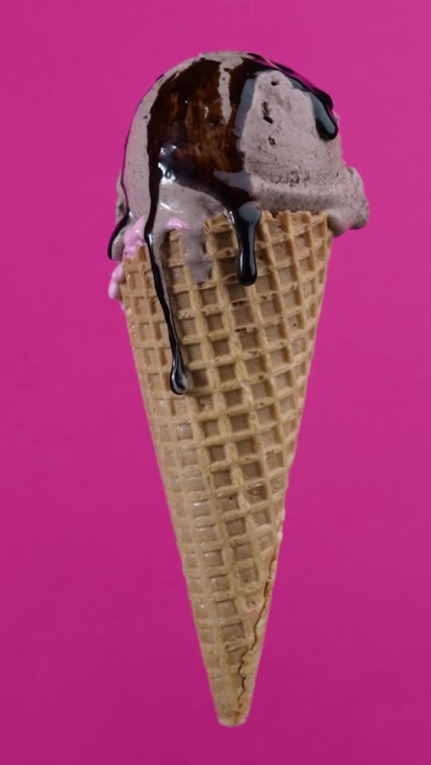 Tasty chocolate ice cream with topping in waffle cone on pink background. Rotating soft cream, gelato icecream scoop in waffle cone over colorful background — ストック動画