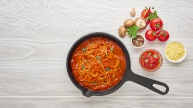 Cinemagraphy cooking homemade pasta with tomato sauce in cast iron pan served with chili pepper, fresh basil, cherry-tomatoes and spices over white texture wooden background, ingredients food concept