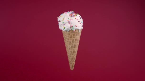 Vanilla ice cream in waffle cone. Sweet dessert decorated with colorful sprinkles, rotating soft cream, gelato icecream scoop on red background — Wideo stockowe