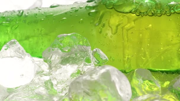 Green glass bottle of cold lager beer chilling on ice cubes, low angle, side view, water drops on glass, refreshing frozen alcoholic beverage with splashes over ice background close up in slow motion — Wideo stockowe