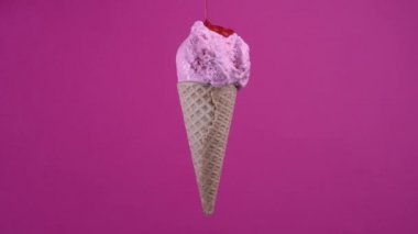 Rotating ice cream in waffle cone and pouring strawberry topping. Sweet dessert decorated with colorful sprinkles, soft cream, gelato icecream scoop over pink background