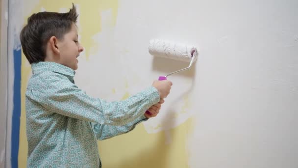 Bonito menino engraçado da escola fazendo renovação, decorando sala de pintura de uma parede com uma escova de rolo de pintura. Criança inteligente focada desfrutando de atividade de hobby de arte criativa em casa, conceito de desenvolvimento infantil — Vídeo de Stock