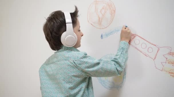 Χαριτωμένο αστείο σχολείο παιδί αγόρι καλλιτέχνης σε ακουστικά σχέδιο χρωματισμός εικόνα με κιμωλία, κηροπήγιο σε λευκό τοίχο, επικεντρώθηκε έξυπνο παιδί απολαμβάνοντας δημιουργική δραστηριότητα χόμπι τέχνης στο σπίτι, τα παιδιά έννοια ανάπτυξης — Αρχείο Βίντεο
