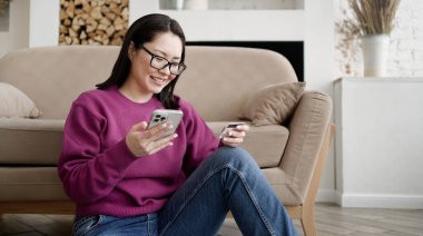 Asyalı bayan müşterinin elinde banka kartı ve mobil uygulama doğrulama sürecine dahil akıllı telefon var. İnternet üzerinden ödeme yapan ya da internetten alışveriş yapan mutlu bir kadın.