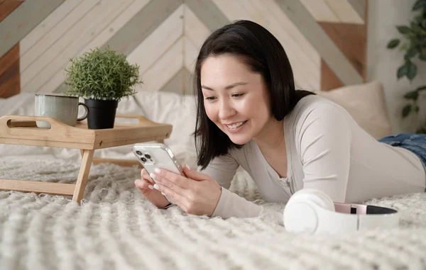 Genç Asyalı kadın sosyal medyada akıllı telefon sörfü yapıyor, haberleri kontrol ediyor, mobil oyunlar oynuyor ya da koltukta oturmuş mesaj yazıyor. Karışık ırk hanımı evinde cep telefonu teknolojisiyle vakit geçiriyor..