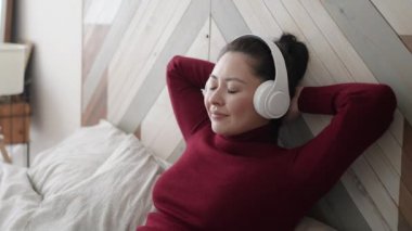 Genç ve çekici Asyalı kadın rahat koltukta, gözleri kapalı, kulaklık takıyor. Oldukça sağlıklı sakin bir kız, dinlenmeyi sever. Soğuk müzik sesi, meditasyon, evde stres yok..