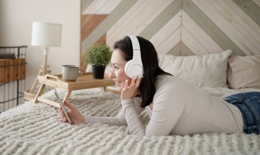 Genç Asyalı kadın sosyal medyada akıllı telefon sörfü yapıyor, haberleri kontrol ediyor, mobil oyunlar oynuyor ya da koltukta oturmuş mesaj yazıyor. Karışık ırk hanımı evinde cep telefonu teknolojisiyle vakit geçiriyor..