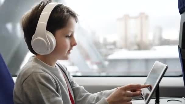 子供は電車で旅行したり、漫画を見たり、窓のそばに座ってタブレットPCでゲームをしたりします。家族の休暇に高速急行列車で学校の少年,若い乗客のためのエンターテイメント. — ストック動画