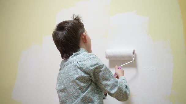 Cute funny school child boy making renovation, decorating room painting a wall with a paint roller brush. Focused smart kid enjoying creative art hobby activity at home, children development concept — Stock Video