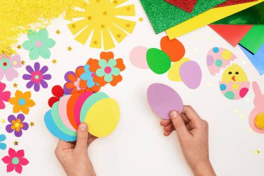 Renkli Paskalya yumurtaları, çiçekler, güneş, tavuk, çok renkli kağıtlardan tavşan, adım adım. Çocuk kendi elleriyle el sanatları yapıyor. Paskalya Bayramı el yapımı sanat yaratıcılığı. Üst görünüm, alanı kopyala