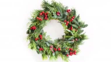 Doğal yeşil dalları ve kutsal böğürtlenli Noel çelengi yavaş çekimde dönüyor.. 