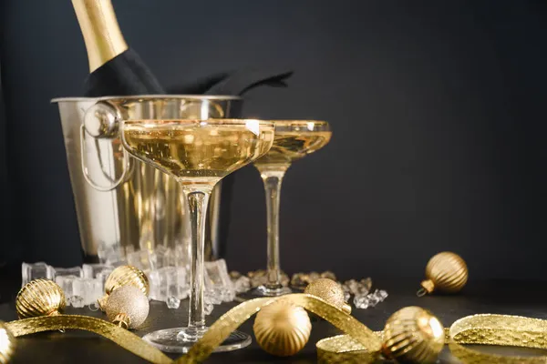 Πρωτοχρονιά σαμπάνια σε ποτήρια κρασιού και μπουκάλι σε κουβά διακοσμημένα Χριστούγεννα χρυσά μπιχλιμπίδια. — Φωτογραφία Αρχείου