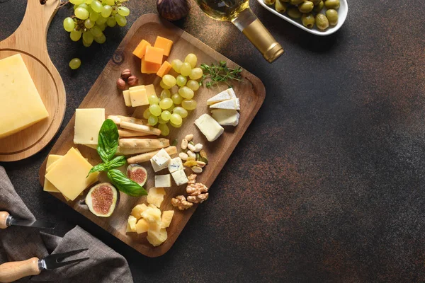 Cheese platter with grapes, nuts, figs, white wine on a brown background. Top view. Copy space. Appetizer for festive party.