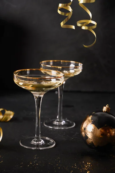 Πρωτοχρονιάτικα ποτήρια σαμπάνιας και χριστουγεννιάτικες χρυσές διακοσμήσεις σε μαύρο φόντο. — Φωτογραφία Αρχείου