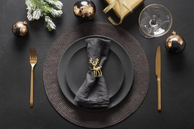 Koyu siyah tabaklar, altın geyik yüzüğü ve altın çatal bıçaklı Noel sofrası. Altın yaldızlı süslemeler.