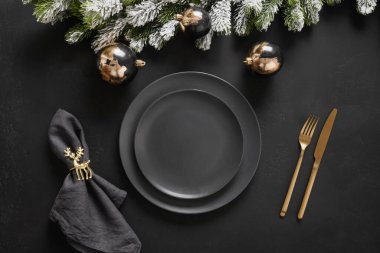 Koyu siyah tabaklar, altın geyik yüzüğü ve altın çatal bıçaklı Noel sofrası. Altın yaldızlı süslemeler.