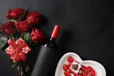 Valentine's day gift, red wine, bouquet of roses on black background. Greeting card with copy space. View from above.