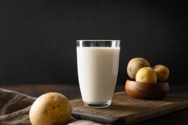 Kahverengi arka planda vegan patates sütü ve patates. Kapatın. Bitki bazlı süt değiştirici ve laktozsuz.