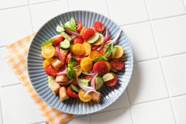 Piquant Panzanella with tomatoes, bread, cheese in blue plate on white kitchen background. Top view. Italian cuisine. Summer vegetables colorful vegan panzanella salad.