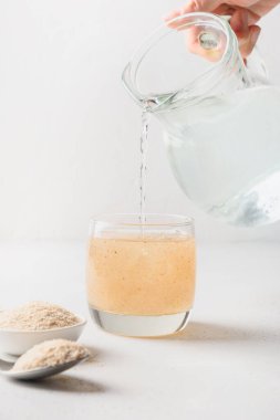 Kadın beyaz arka planda bir bardak suya psyllium lifleri ekliyor..