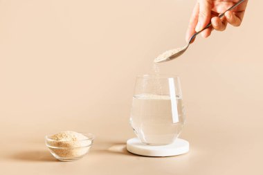 Kadın beyaz arka planda bir bardak suya psyllium lifleri ekliyor..
