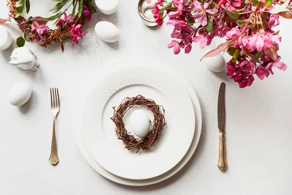 Osteressen mit Eiern, Hasen, festlichem Geschirr und Tulpen auf Weiß. — Stockfoto