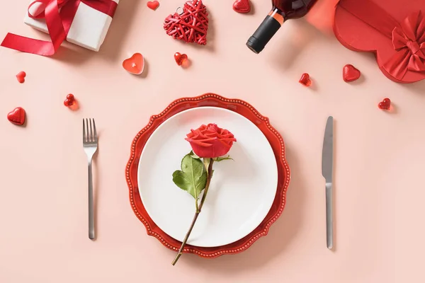 День святого Валентина место накрытия стола с подарком, бутылка красного вина, розы, сердца. — стоковое фото