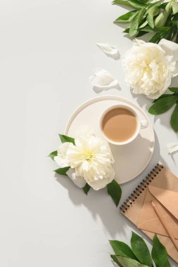 Kahve fincanı ve gri ofis masasında beyaz şakayık çiçekleri olan romantik yaz kahvaltısı..