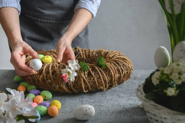 Mujer haciendo corona floral de Pascua de materiales naturales de flores y huevos. — Foto de Stock