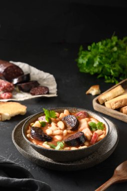 Sucuklu, pastırmalı, sosisli, haricot sosisli Asturiana fabada siyah masada taze kızarmış ekmek servis etti. Dikey oryantasyon. Lezzetli geleneksel İspanyol yemeği..