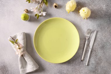 Yeşil tabaklı Paskalya sofrası, bahar çiçekleri ve gri arka planda yeşil yumurtalar. Yukarıdan bak. Metin için boşluk.