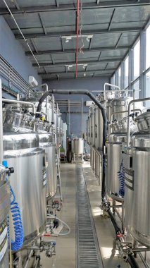 Row of shiny metal micro brewery tanks or Fermentation mash vats in Brewery factory. Modern beer plant with brewering kettles, tubes and tanks made of stainless steel