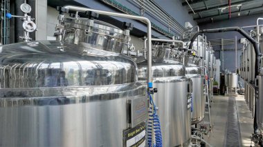 Row of shiny metal micro brewery tanks or Fermentation mash vats in Brewery factory. Modern beer plant with brewering kettles, tubes and tanks made of stainless steel